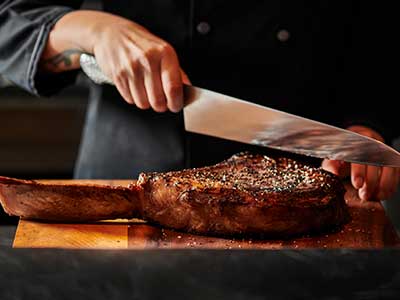 The 35oz prime tomahawk ribeye as the chef holds a large knife over it