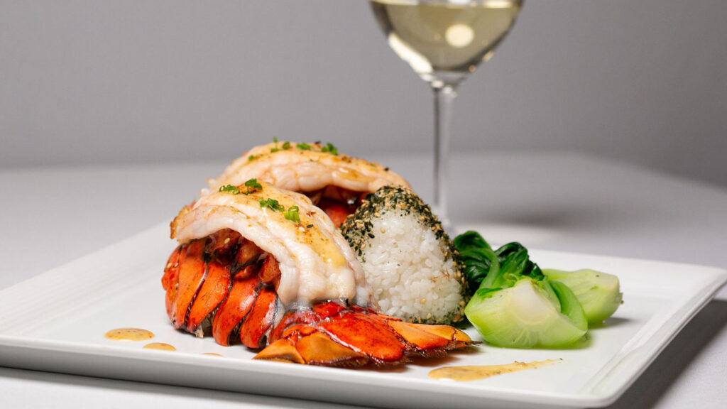 Roys restaurant dish with twin lobster tails and white wine in glass in background