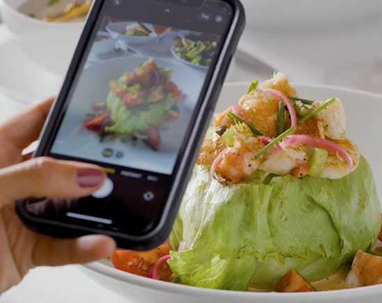 Guest capturing a photo on their phone of the shellfish louie seafood salad at Fleming's Prime Steakhouse